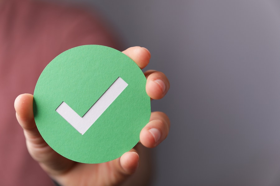 A Hand Holding A Green Paper With The Checkmark Sign On It.