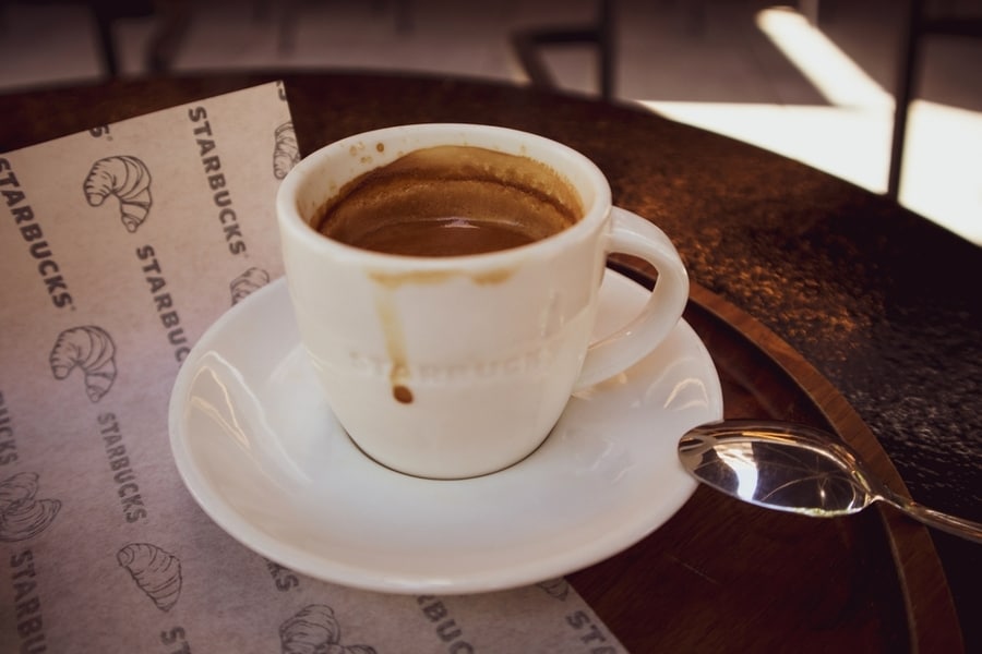 A White Ceramic Cup Of Freshly Brewed Coffee, Cappuccino, Espresso Stands On A Round Brown Table At A Coffee Shop Terrace In A Starbucks Fast Food Restaurant.