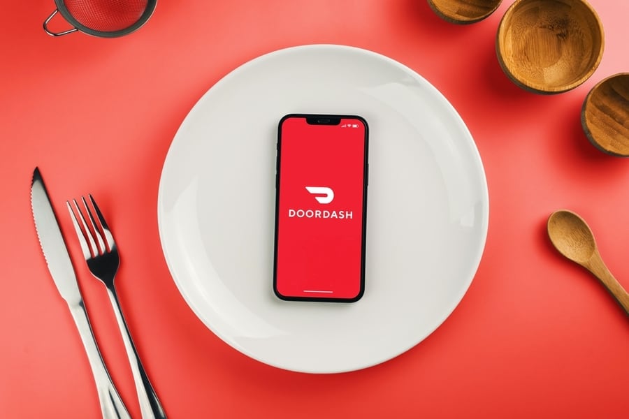 Doordash Delivery App On Smartphone Screen On Top Of White Plate. Beside Cutlery And Utensils.