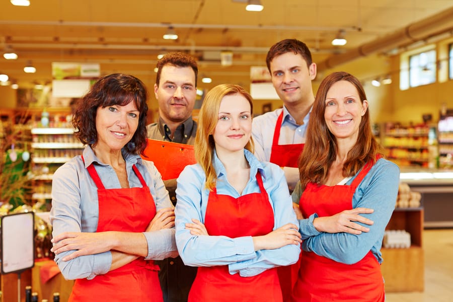 Team Of Five Happy Salespeople Together In A Supermarket With Their Arms Crossed