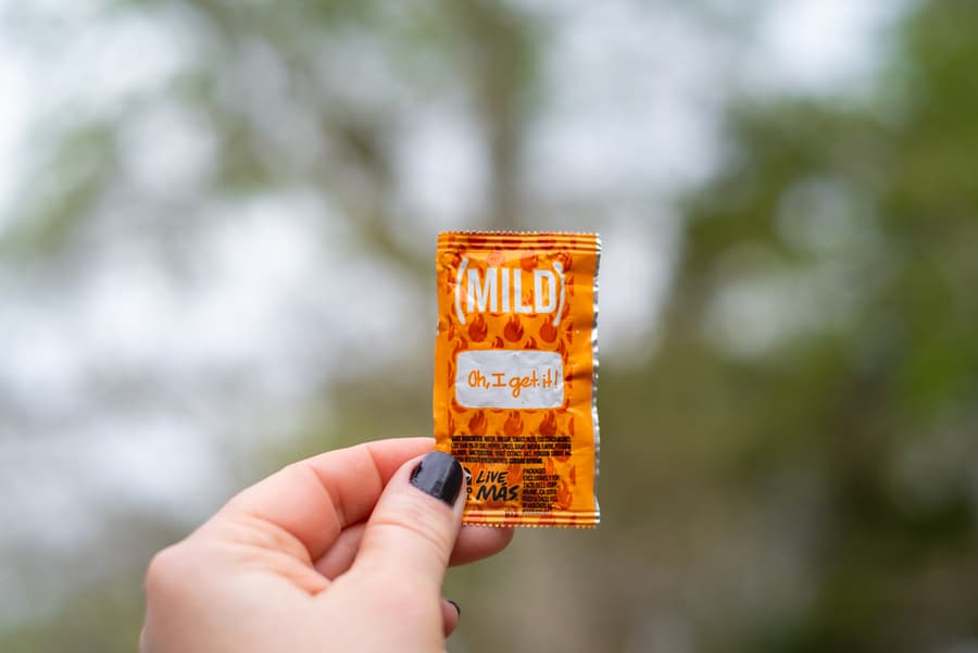 A Closeup View Of A Caucasian Lady's Hand, Holding A Small, Orange Packet Of Taco Bell Mild Sauce, Outdoors, During The Spring, In South Louisiana.