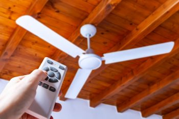 A Person Using A Remote Control To Operate A Ceiling Fan Mounted In A House On A Wooden Ceiling.