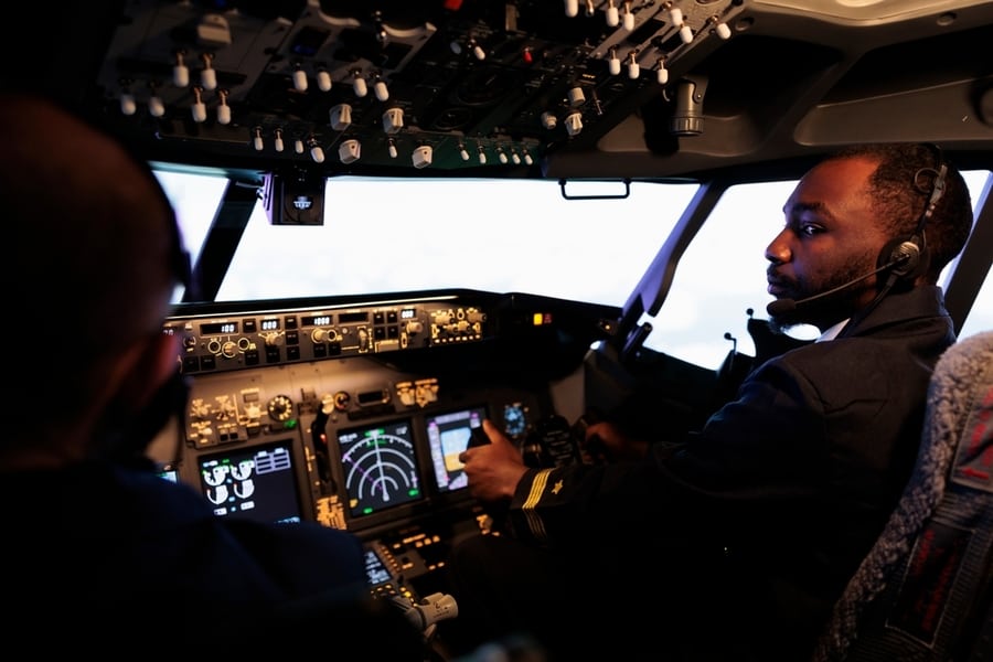 African American Pilot Flying Aircraft Jet Doing Teamwork With Captain, Using Dashboard Command And Navigation. Team Of Airliners Pushing Control Panel Buttons And Lever To Takeoff And Fly.