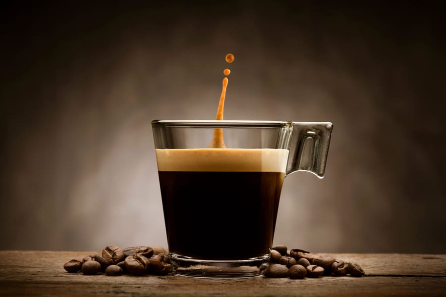 Black Coffee In Glass Cup With Coffee Beans And Jumping Drop