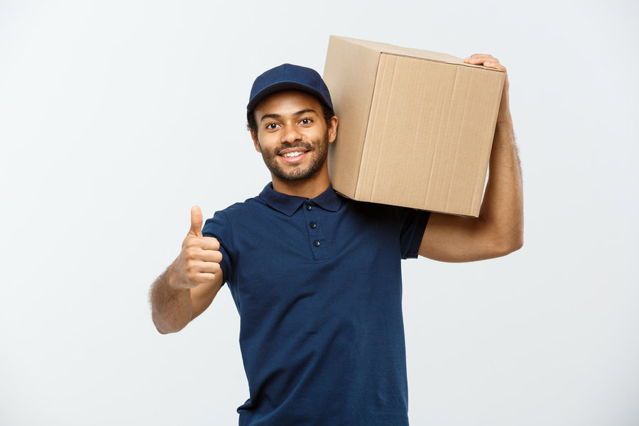 Delivery Concept - Portrait Of Happy African American Delivery Man Holding A Box Package And Showing Thumbs Up. Isolated On Grey Studio Background.
