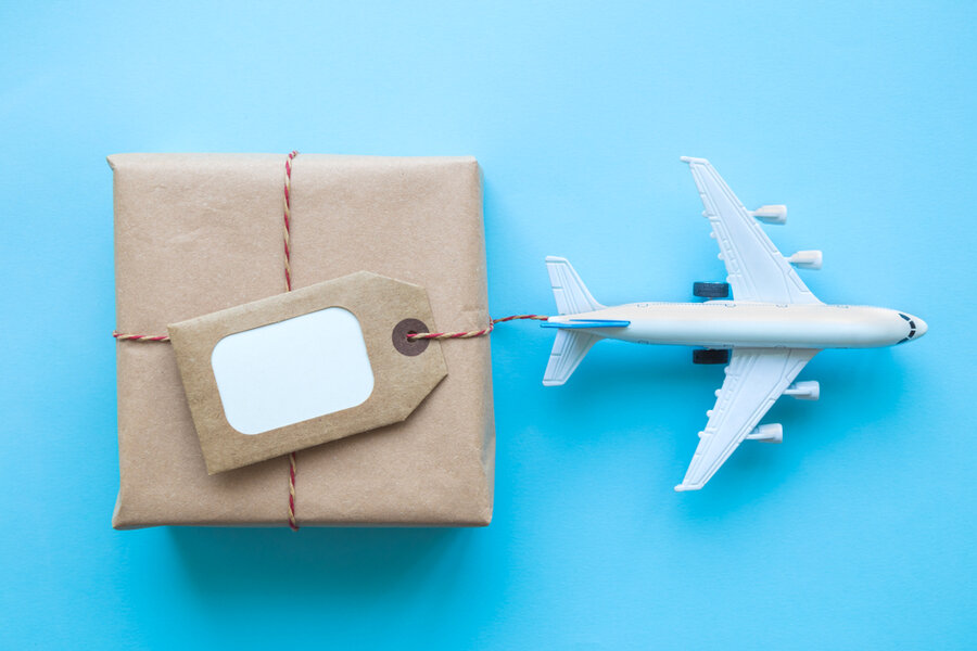 Flat Lay Of Wrapped Package With Blank Tag And Airplane Model On Pastel Blue Background.