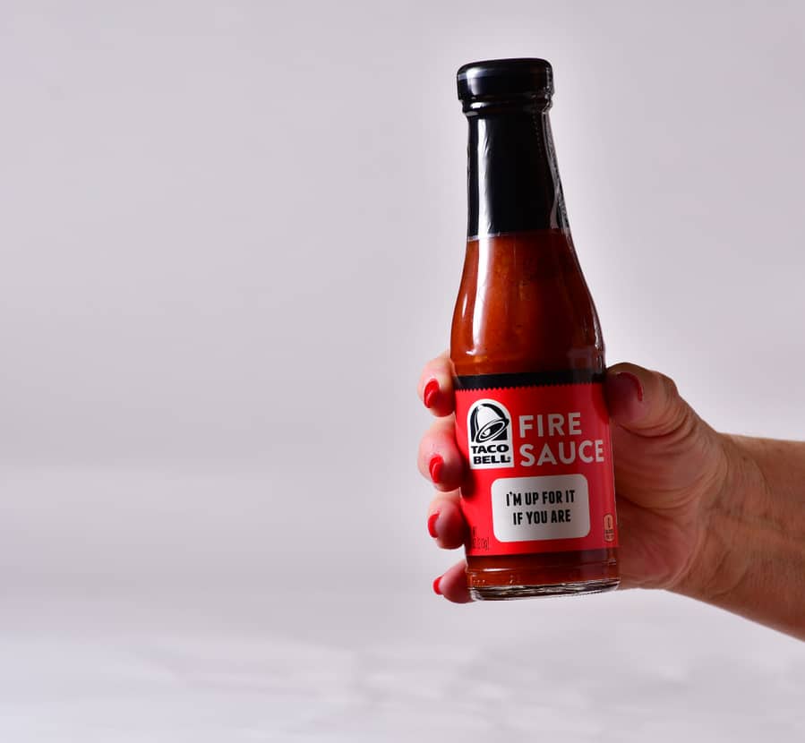 Middle Aged Caucasian Woman With Red Fingernails Holding A Bottle Of Taco Bell Brand Fire Sauce