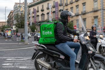 Uber Eats, A Boy With A Scooter With The Typical Green Backpack, Delivers Food At Home