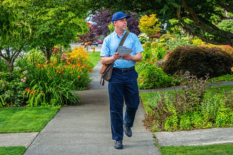 Worker Delivering Mail While Walking Down A Sidewalk In A Upscale Neighborhood