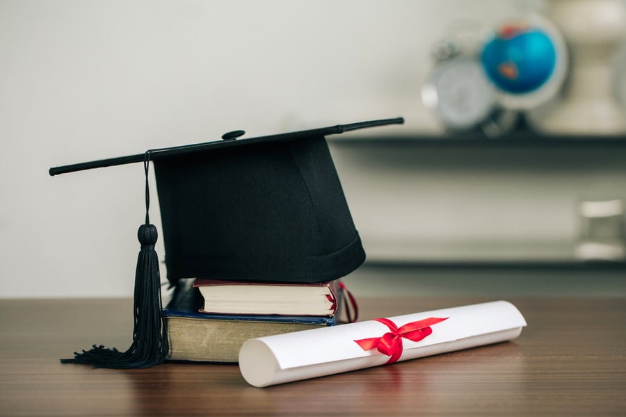 A Mortarboard On Books And Graduation Scroll On The Desk