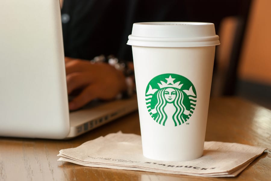A Tall Starbucks Coffee In Front Of A Woman Working On A Laptop Computer
