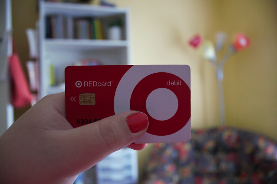 A Woman With Pink Nails Holds A Target Redcard Debit Card In Front Of Her Colorful Bedroom