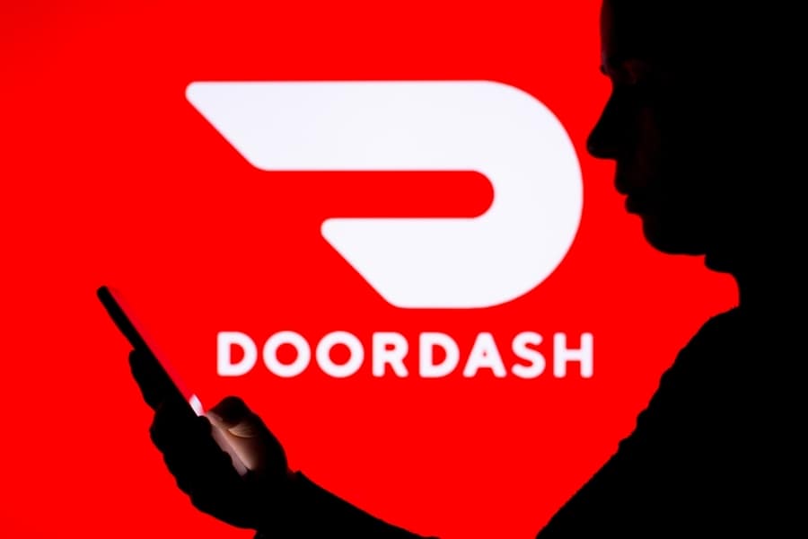 A Woman's Silhouette Holds A Smartphone With The Doordash Logo