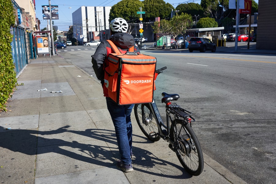 Doordash Delivery Worker Walks His Bike Along The Road