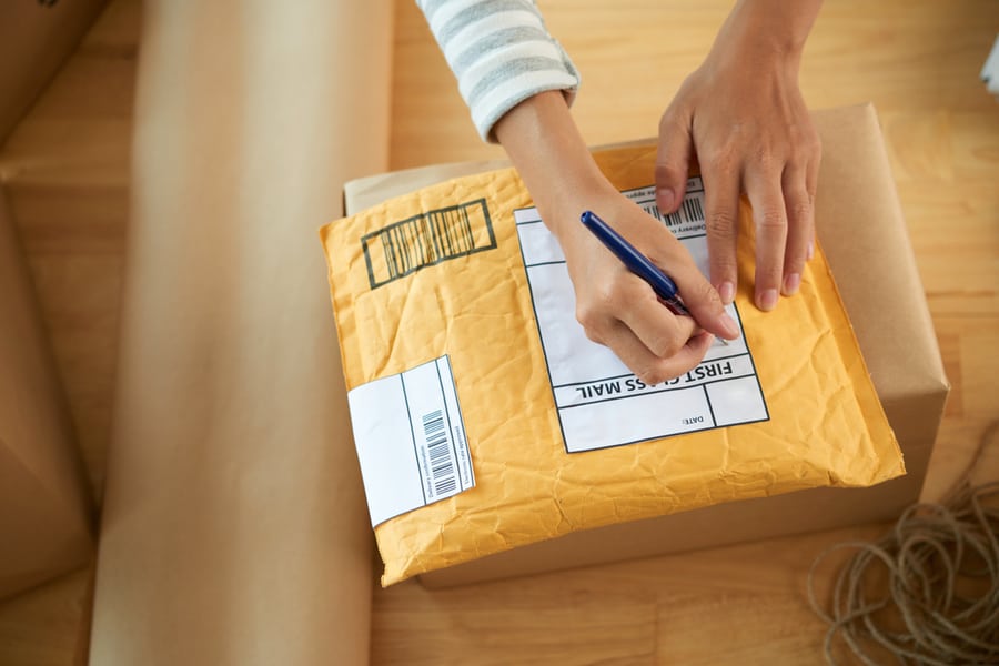 Hands Of Woman Writing Address On First Class Mail Package