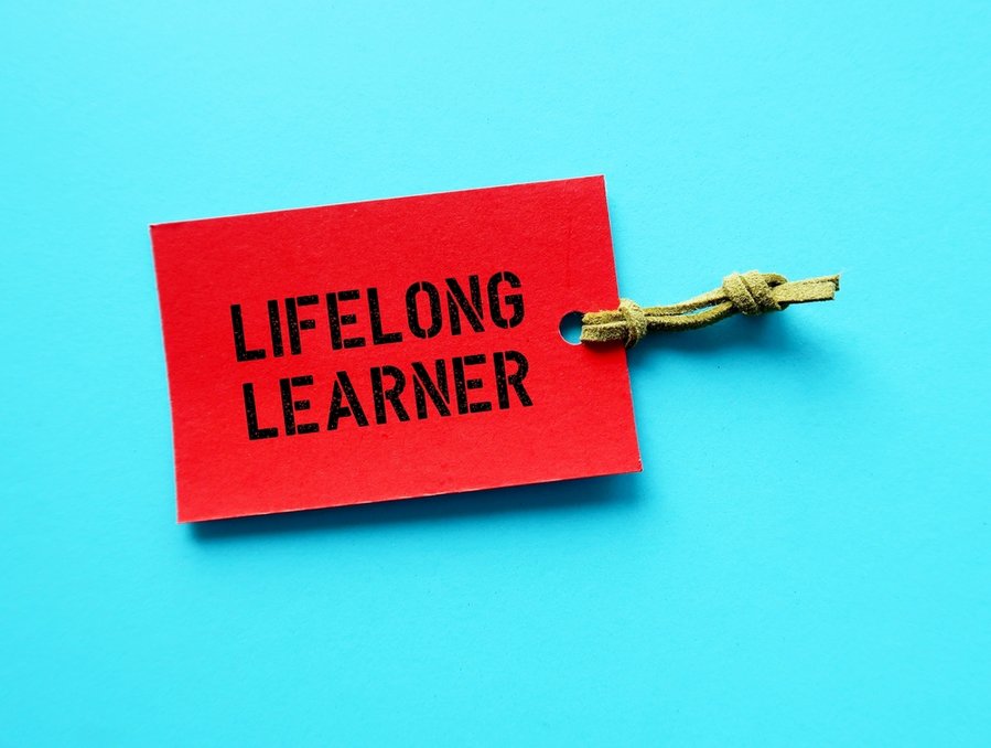 Red Paper Tag On Blue Background With Text Lifelong Learner, People Who Focus On Continual Learning New, In-Demand Skills For Personal Development, Keeps Acquiring New Skills Past Formal Education